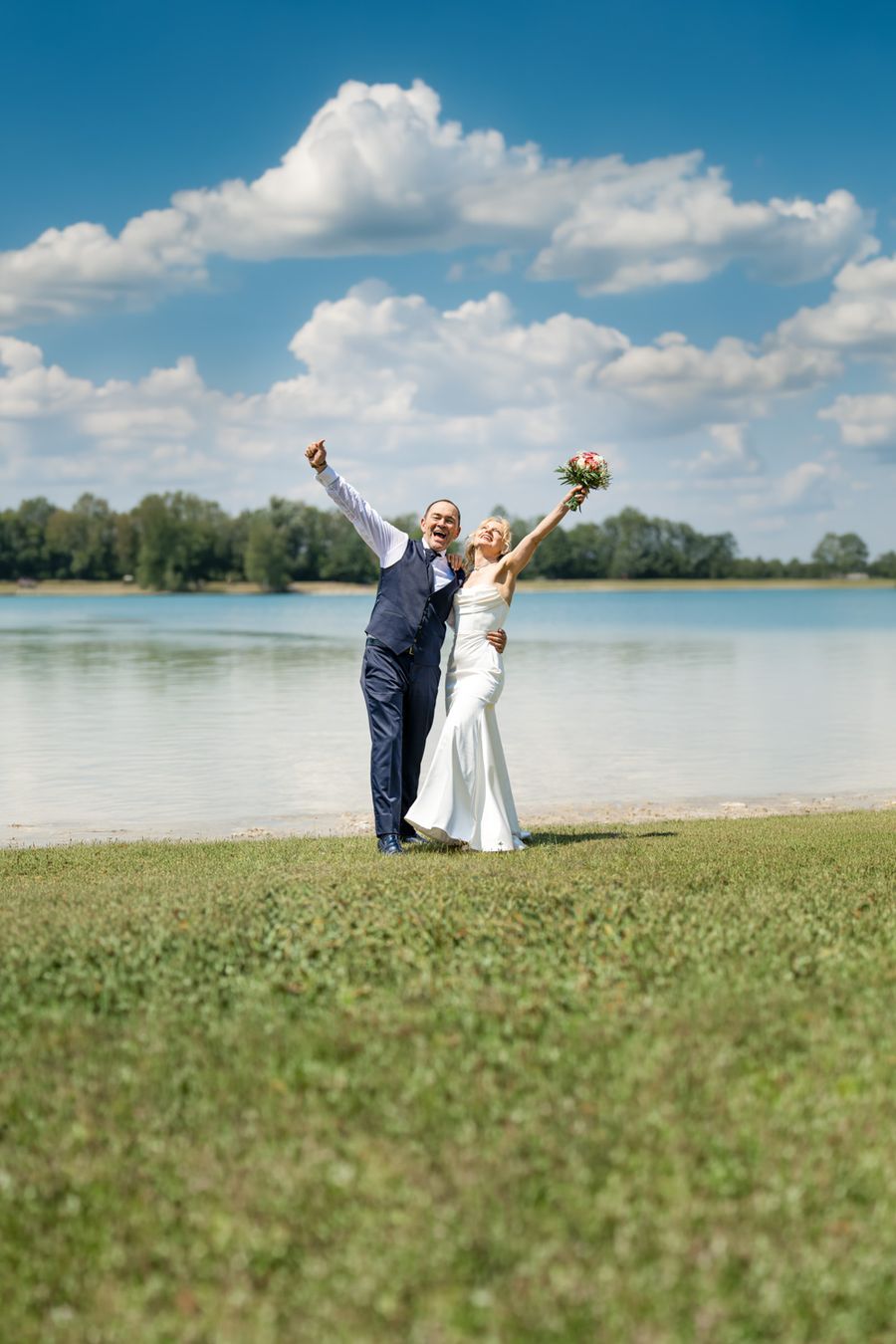 Brautpaar jubelt mit erhobenen Armen am Ufer des Karlsfelder Sees