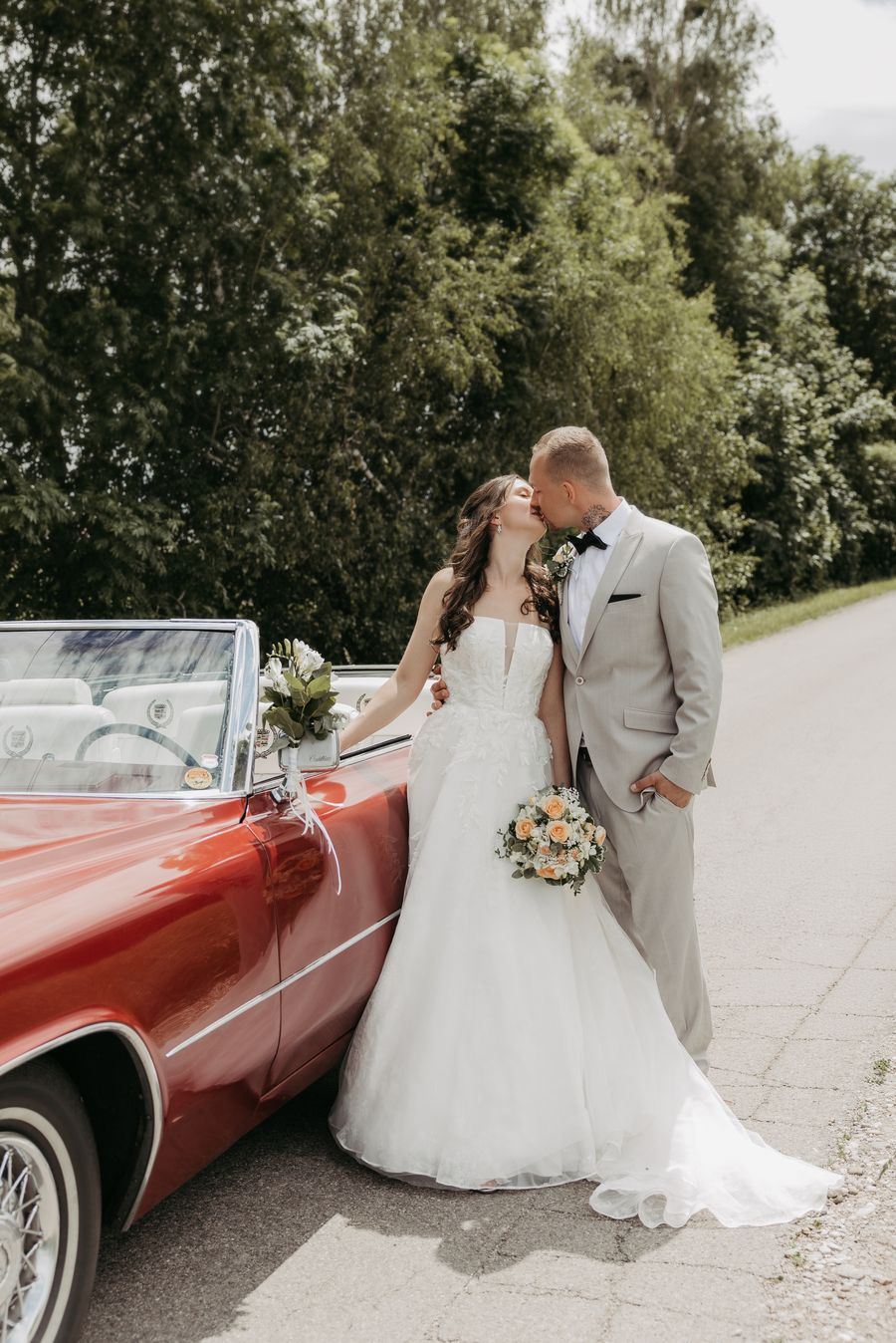 Brautpaar küsst sich vor rotem Oldtimer-Cadillac