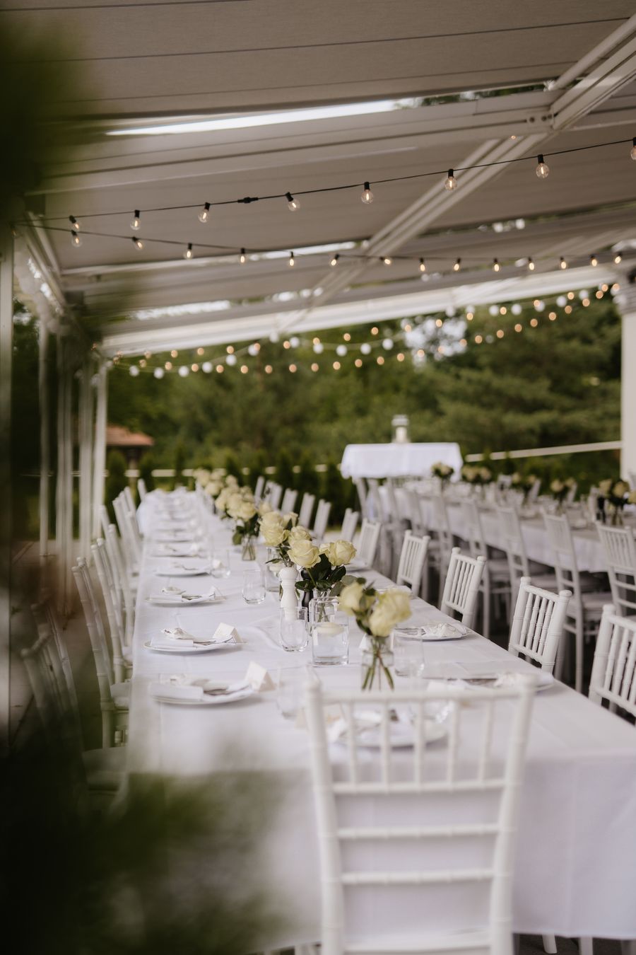 Lange gedeckte Hochzeitstafel unter der Markise der Seeterrasse mit Lichterketten