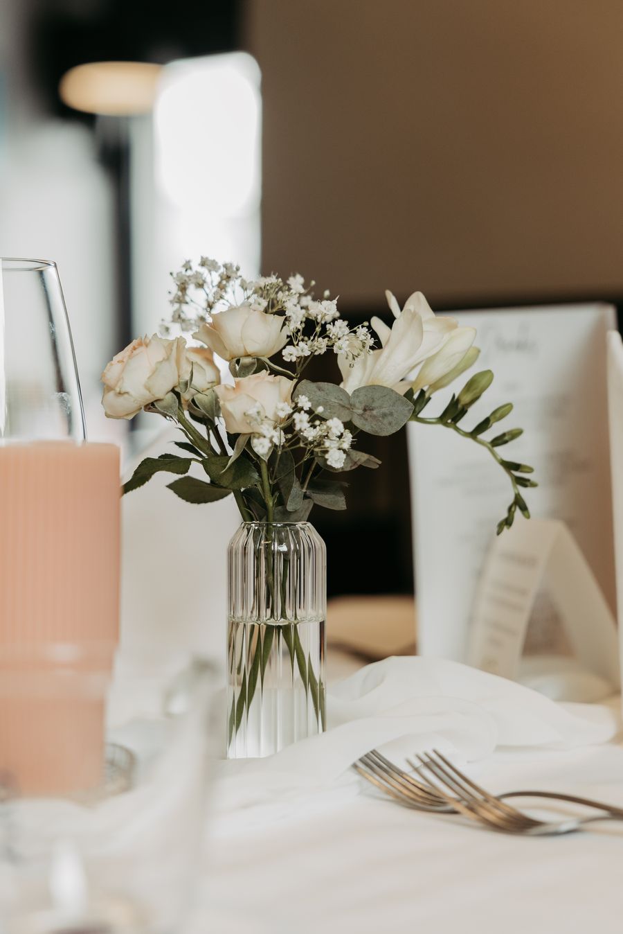Kleine Vase mit Rosen und Freesien auf der Hochzeitstafel